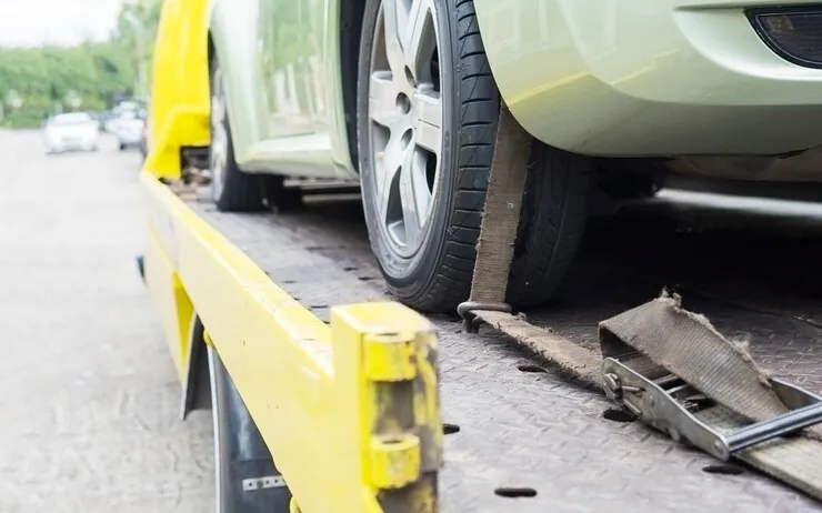 Roata unui autoturism prinsă cu o chingă pe platforma unui evacuator galben